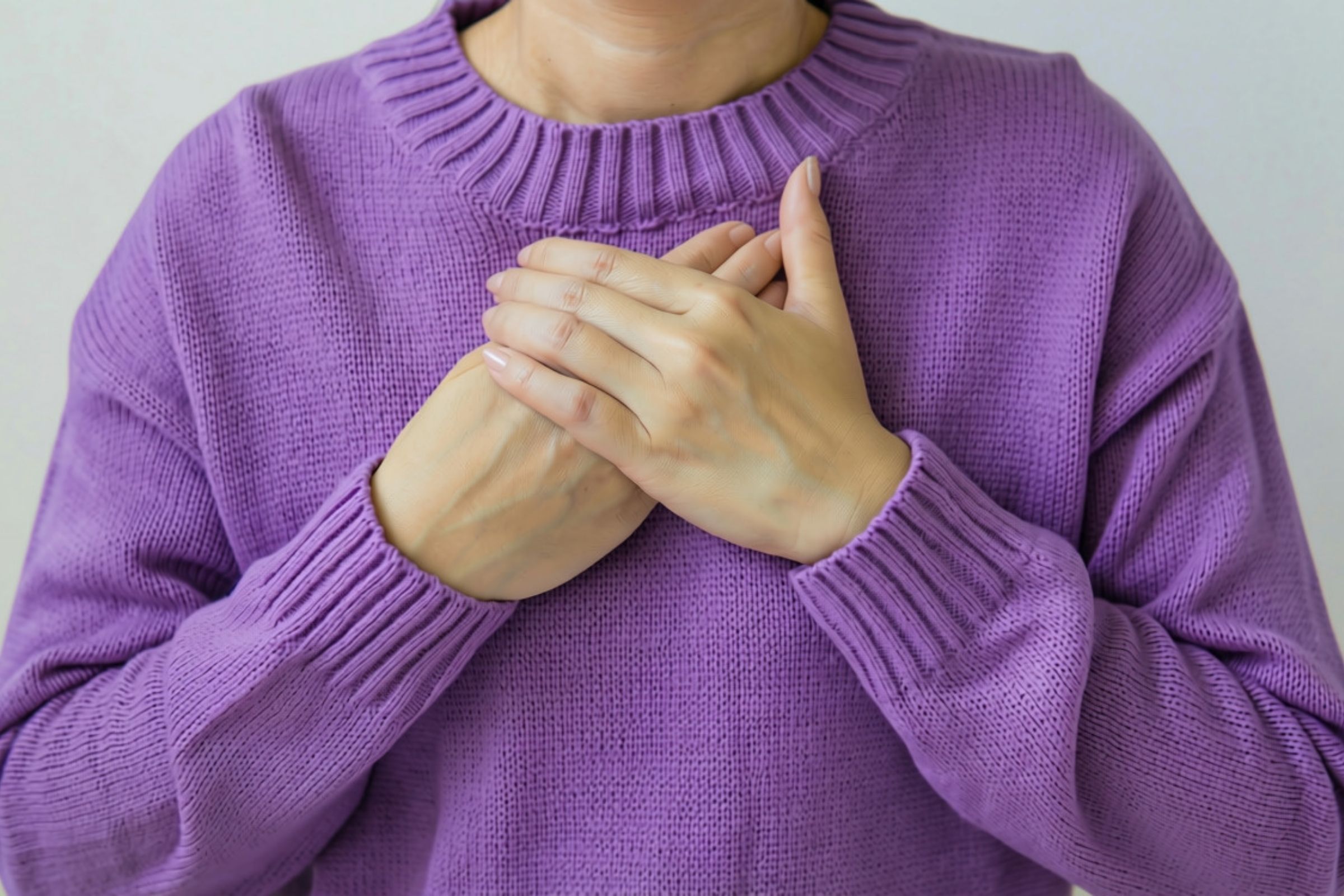 Mains posées sur le cœur Mains posées sur le cœur sur un pull violet
